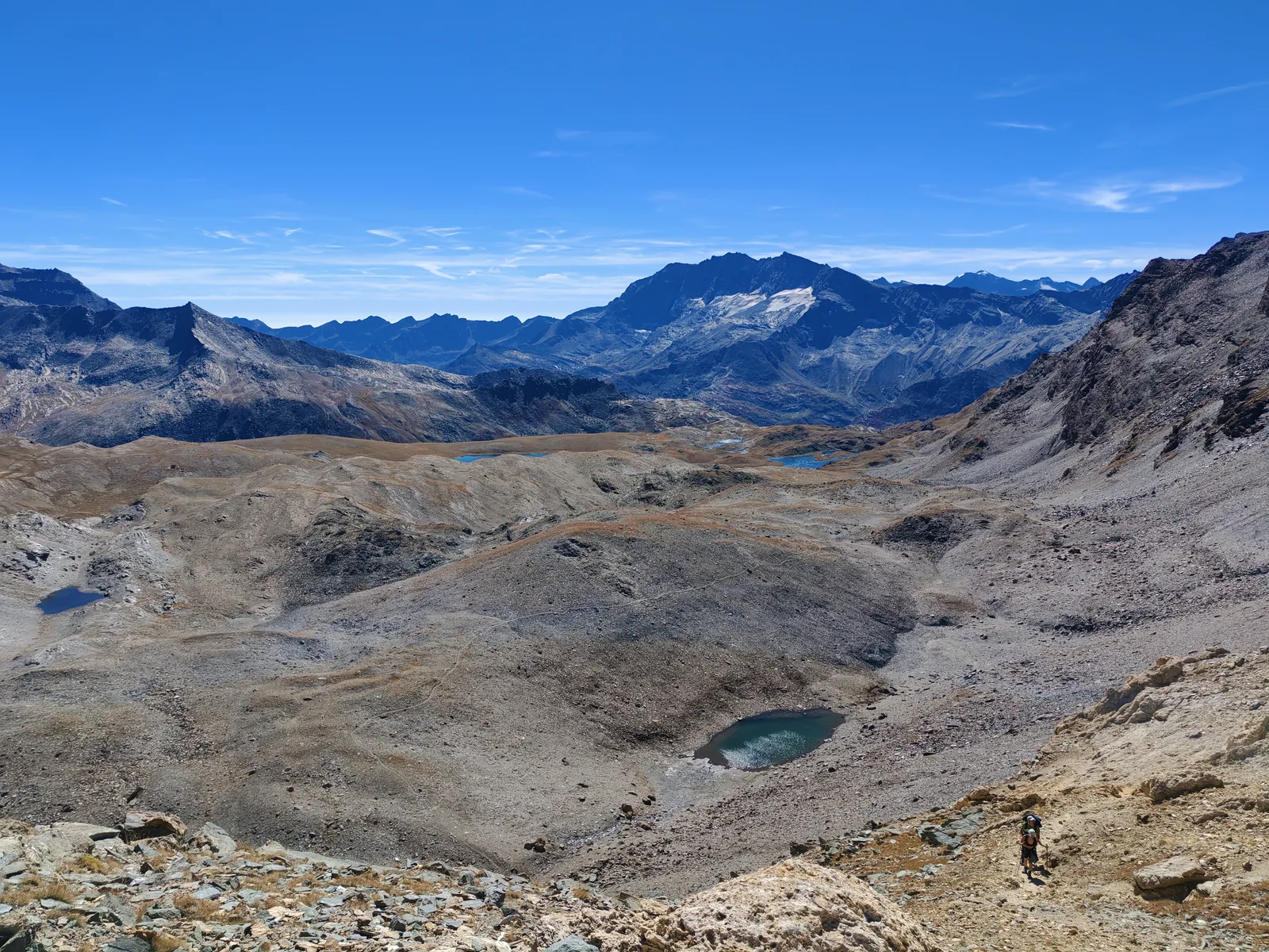 Panorama dal Colle Rosset: una vasta conca detritica con piccoli laghi e, in fondo, le creste glaciali; un escursionista in basso a destra dà la scala