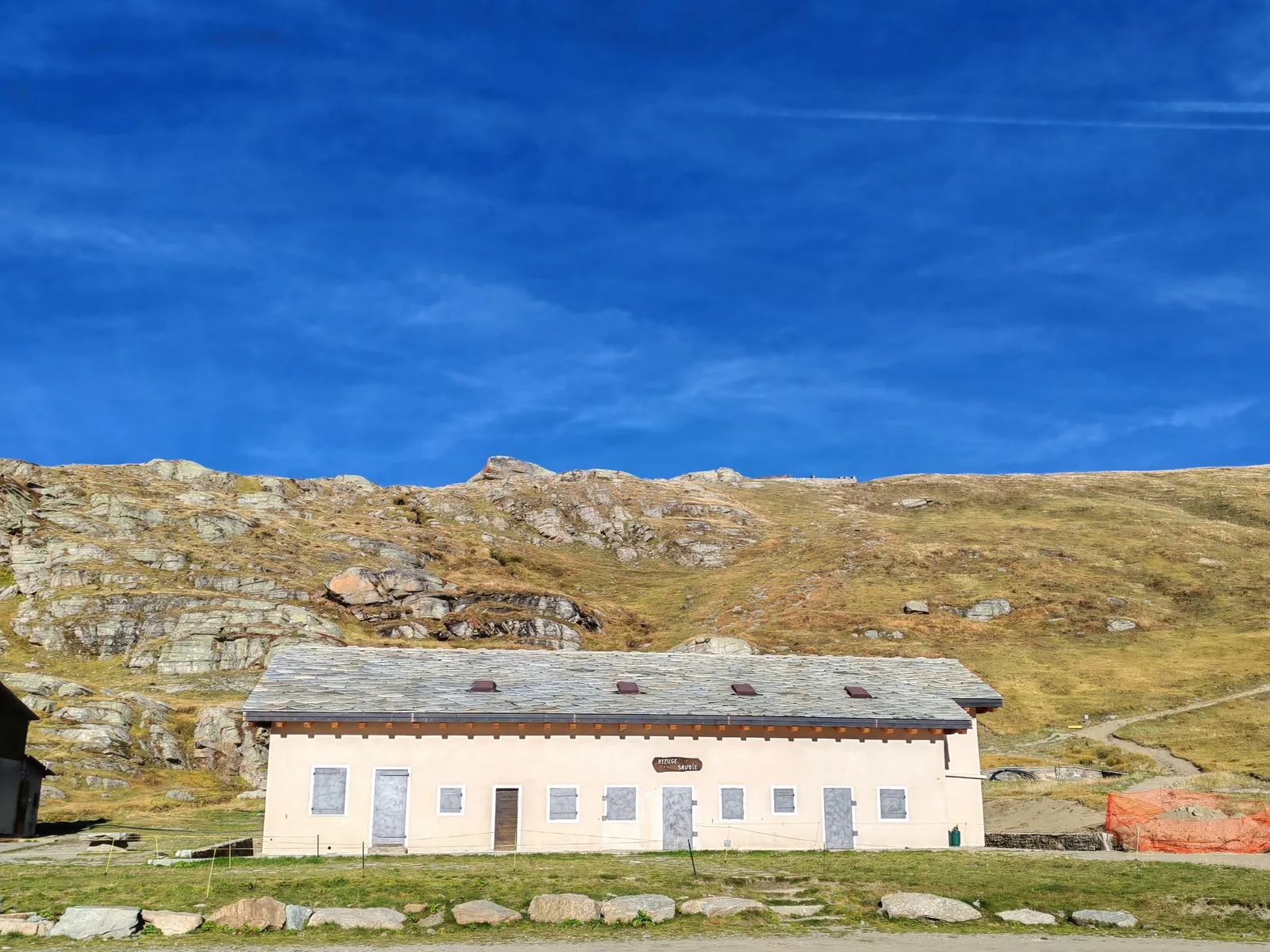 L'edificio storico del Rifugio Savoia con l'insegna «Refuge Savoie», il tetto in lose e il pendio erboso alle spalle