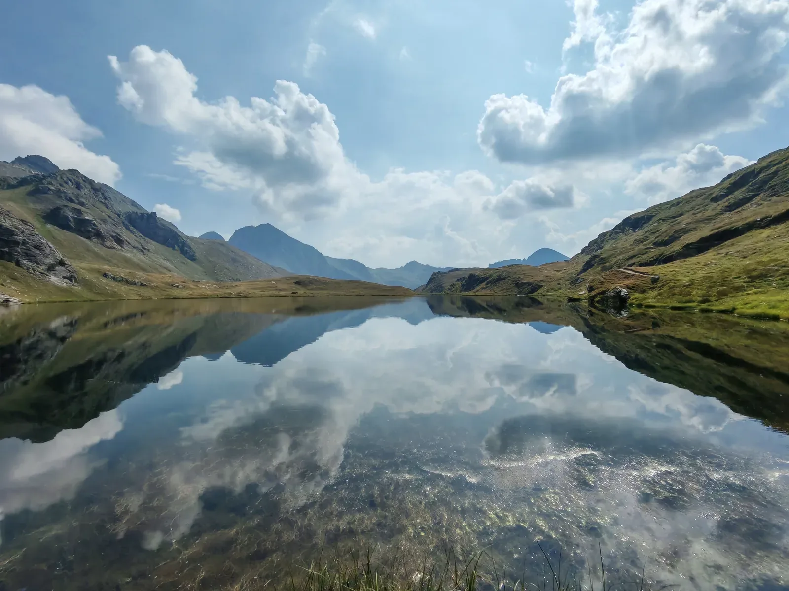 Il Lago della Battaglia perfettamente calmo, con le nuvole riflesse e il fondo sassoso visibile in trasparenza