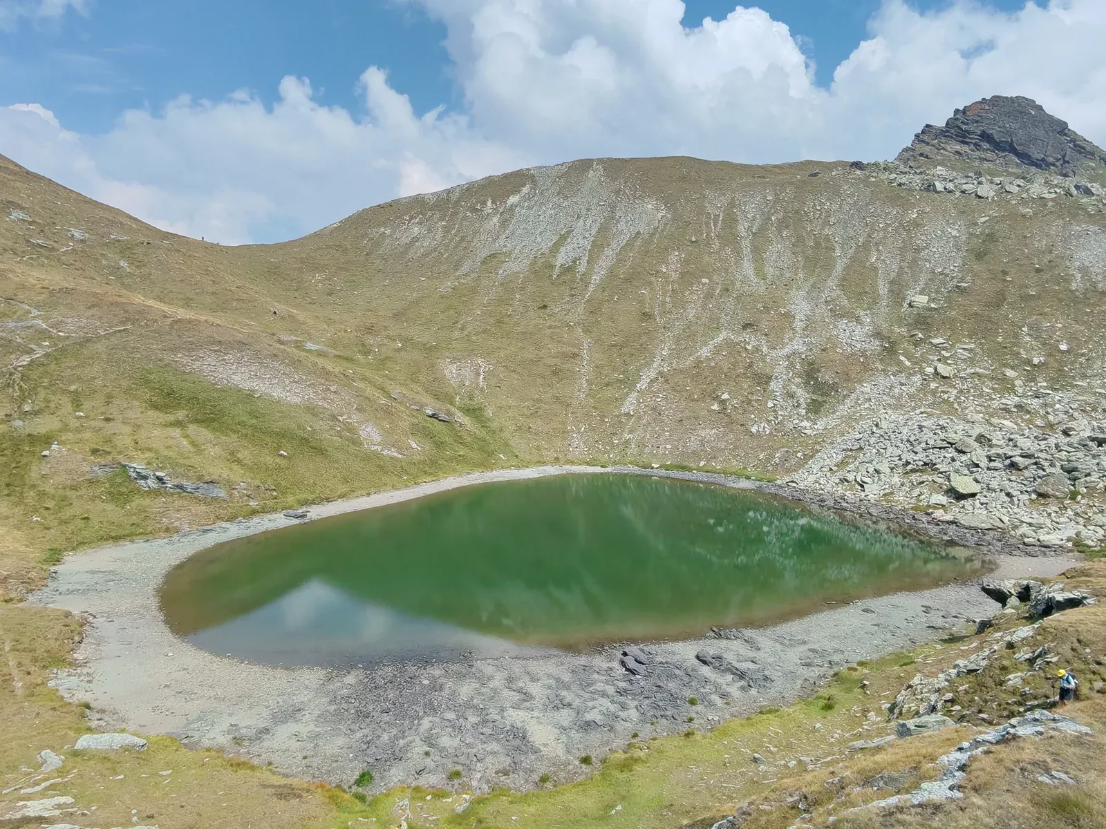 Il Lago di Couloir visto dall'alto, verde, con un'ampia fascia di ghiaia scoperta lungo tutta la riva
