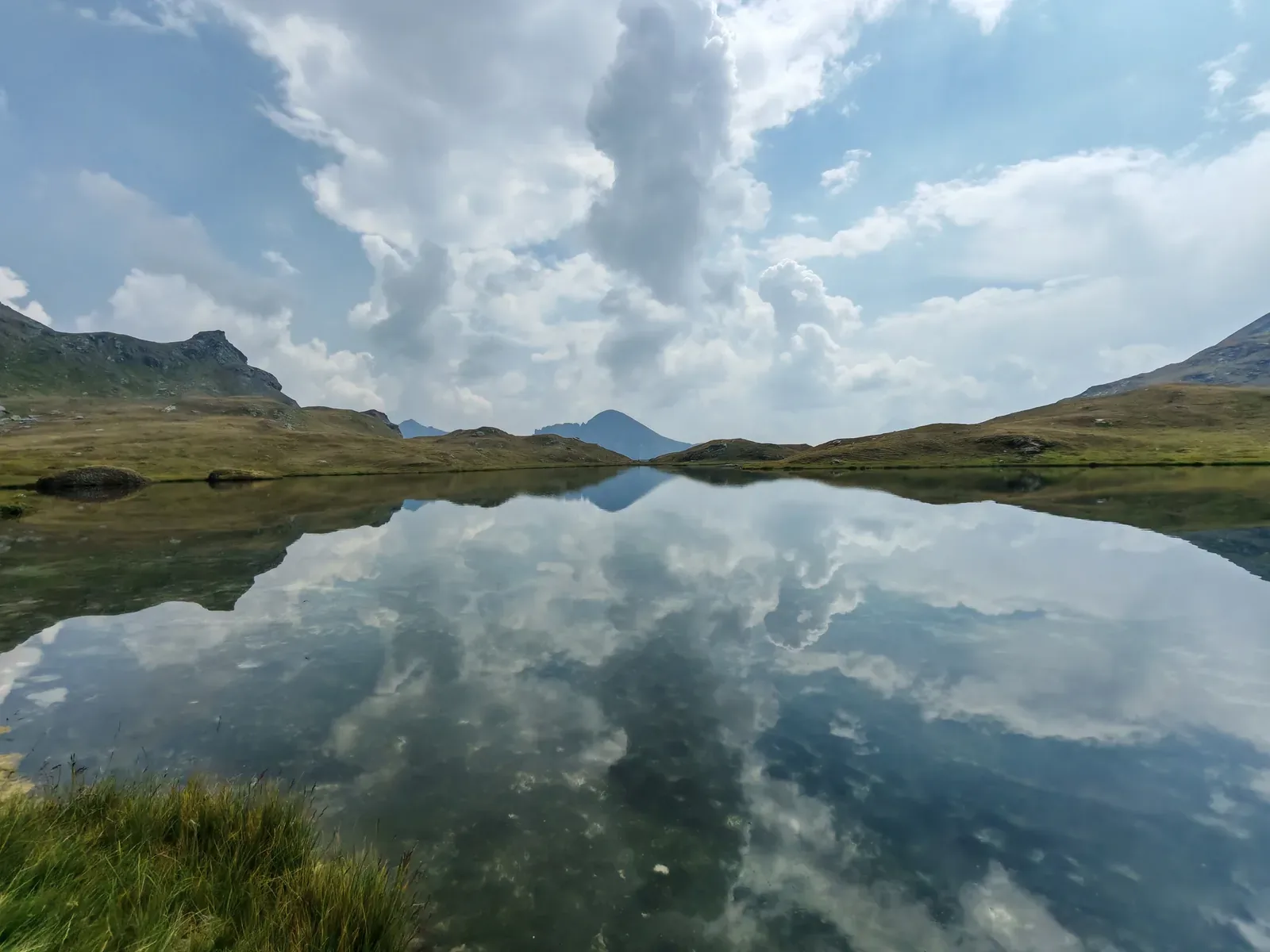 Il Lago Pòtcha come uno specchio, con le nuvole riflesse e le sponde erbose basse