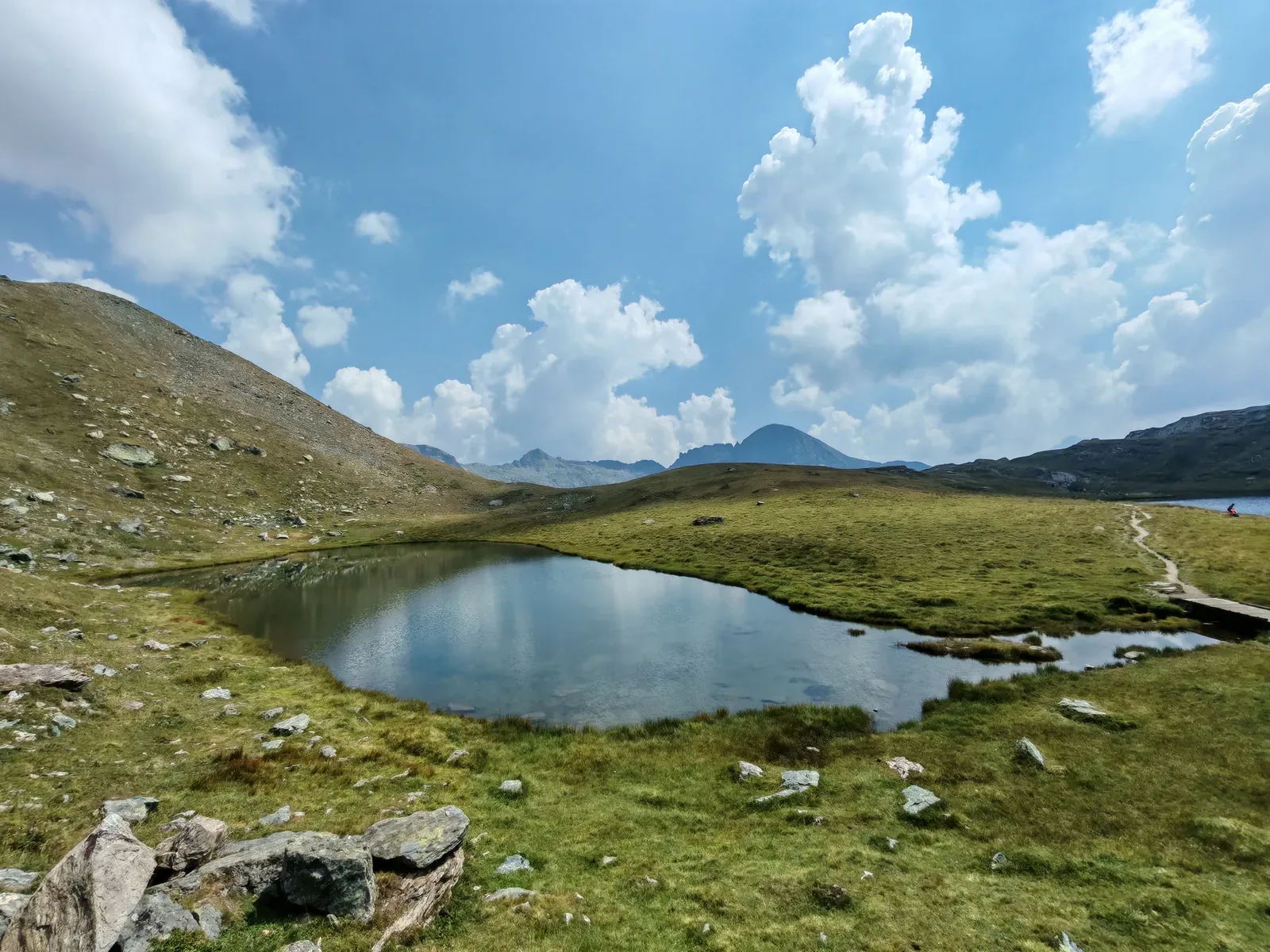 Il piccolo Lago Verde con le sponde a prato, la passerella di legno sulla destra e il Lago della Battaglia sullo sfondo