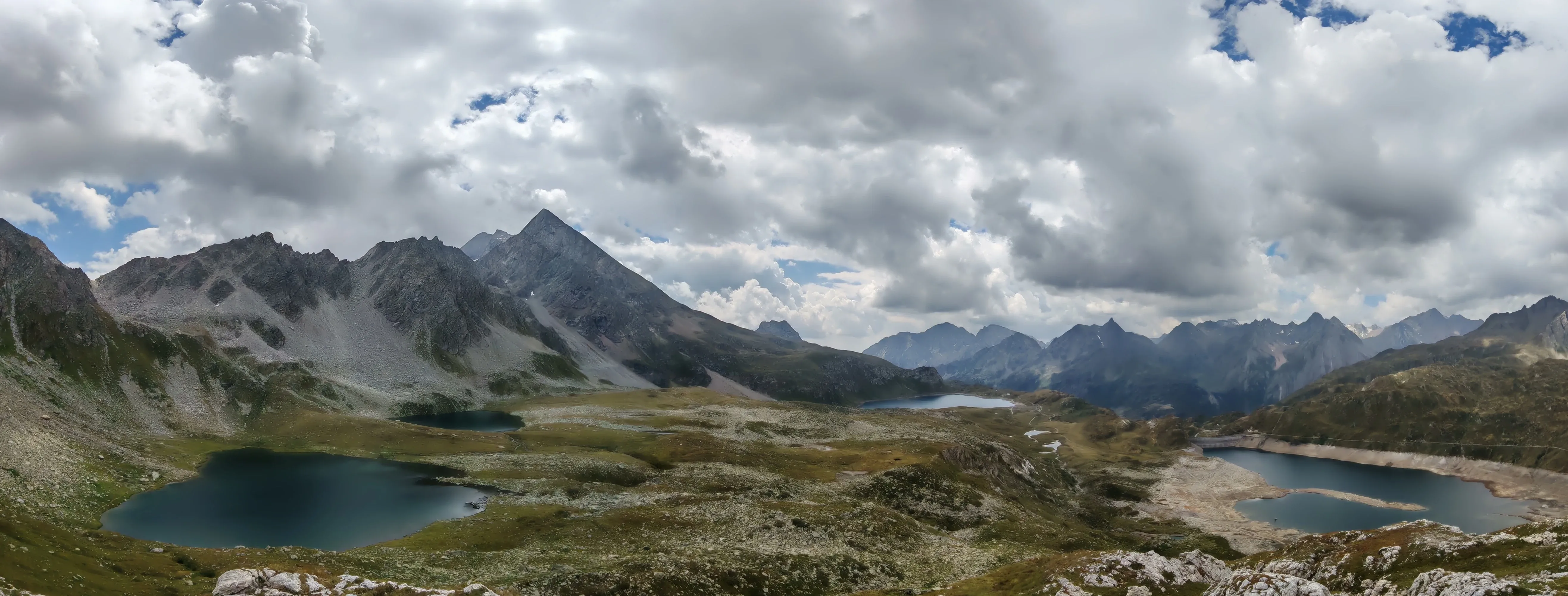 Panoramica del Lago Kastel dal colore turchese, con lo sbarramento a sinistra e le cime dello spartiacque svizzero